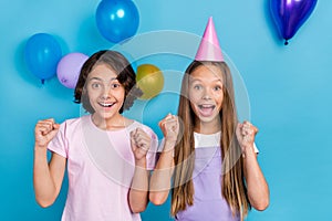 Photo of impressed lucky friends wear casual outfits birthday hats rising fists isolated blue color background