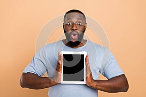 Photo of impressed millennial brunet guy show tablet wear blue outfit isolated on beige color background