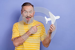 Photo of impressed retired man dressed striped t-shirt directing at white paper plane planing trip isolated on purple