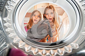 Photo from inside a washing machine where you see two girls putting clothes