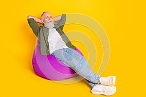 Photo of inspired mature man sit beanbag hands behind head sleep wear green shirt isolated yellow color background