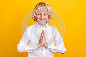Photo of inspired schoolboy close eyes hold palms plead wear school uniform isolated yellow color background