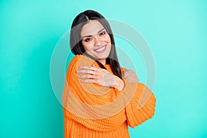 Photo of inspired tender woman embrace herself wear orange sweater  turquoise color background