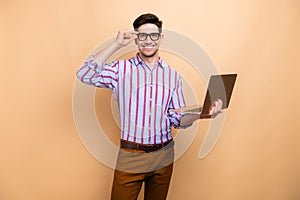 Photo of intelligent entrepreneur male touching his eyeglasses when holding apple macbook laptop isolated on beige color