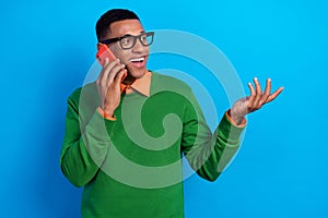 Photo of intelligent handsome man orange shirt under green sweatshirt talk on phone look empty space isolated on blue