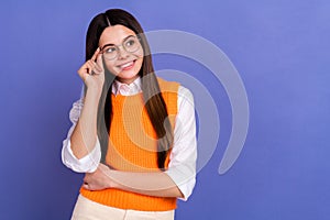 Photo of intelligent satisfied cute schoolgirl dressed orange vest look empty space touch eyewear isolated on purple