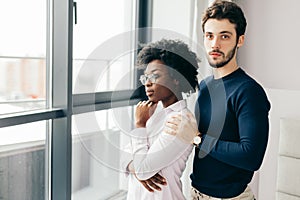 Romantic mixed race couple standing by the window thinking about their future.