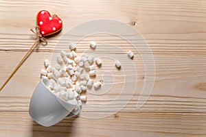 Photo of an inverted cup with marshmallows and a heart with space for copy space. Basis for a greeting card on a wooden background photo