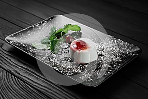 Photo of italian panna cotta dessert with strawberry sirup and mint leaf on the black wooden background.