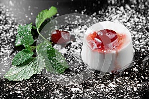Photo of italian panna cotta dessert with strawberry sirup and mint leaf on the black wooden background.