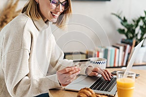 Photo of joyful attractive woman holding credit card and using laptop