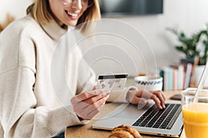 Photo of joyful attractive woman holding credit card and using laptop