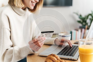 Photo of joyful attractive woman holding credit card and using laptop