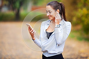 Photo of Joyful Fitness Woman 30s in Sportswear Touching Bluetooth Earpod and Holding Mobile Phone, While Resting in