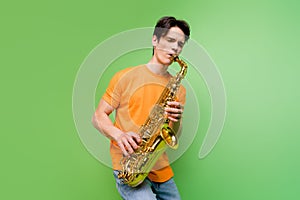 Photo of joyful happy young man hold hands play saxophone jazz lover isolated on green color background