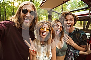 Photo of joyful hippie people men and women, taking selfie in forest near retro minivan