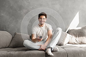 Photo of joyful man 30s in casual clothing sitting on sofa in li