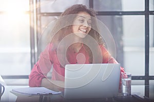 Photo of joyful nice woman using laptop and smiling while sitting photo