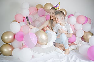 Photo of joyful woman with kid boy smiling and taking selfie photo on cellphone  with balloon. Birthday party