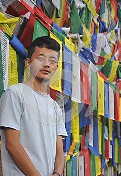 Photo of a Ladakhi young guy looking at camera, standing against Buddhist prayer flags with copy space