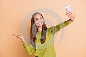 Photo of lady hold phone take selfie arm hold empty space wear green pullover isolated beige color background