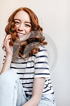 Photo of laughing jocund girl wears vintage blue jeans. Adorable ginger woman in striped t-shirt si