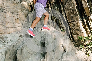 Photo of legs of child climbing up rock in mountains, side view. Little girl in sports shorts and sneakers go down steep