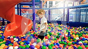 Photo of little boy playing in the pool full of colroful plastic balls. Toddler having fun on playground in shopping