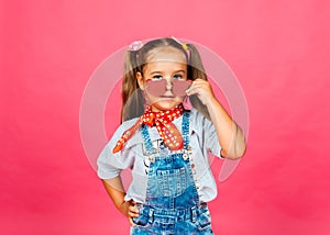 Photo of a little cute beautiful girl standing isolated on a pink background, wearing sunglasses, looking at the camera