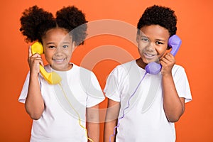 Photo of little funny girl boy talk telephone wear white t-shirt isolated on orange background