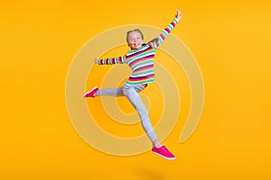 Photo of little girl jump make modern dance move wear striped shirt jeans sneakers isolated yellow color background