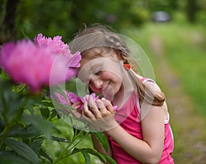 A photo of a little girl smelling big bright flowers with her eyes closed