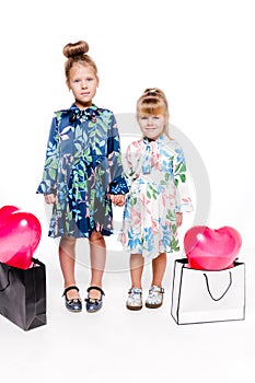 2 little girls with elegant dresses hold large bags with heart-shaped balloons inside