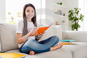 Photo of little pretty pupil school girl lady writing copy book diary homework diligent student sit sofa homey domestic