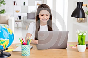 Photo of little pretty pupil small school lady turn on skype laptop notebook online lesson video call sitting table desk photo