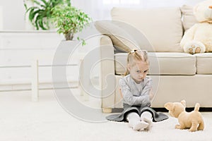 Photo of little sad girl sitting on carpet.