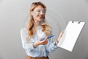 Photo of lovely blond secretary woman with long curly hair writing down notes in clipboard while working in office