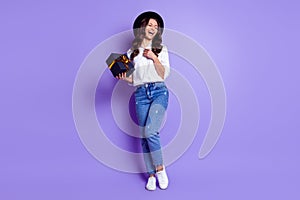 Photo of lovely lady hold box laugh hand chest wear hat white shirt jeans footwear isolated purple color background