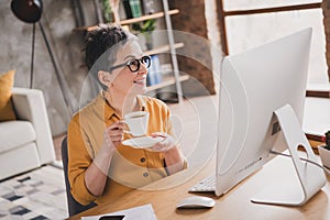 Photo of lovely mature lady sit table drink coffee dressed yellow formalwear modern workplace success business owner