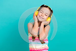 Photo of lovely peaceful small girl closed eyes arms touch headphones favorite song isolated on teal color background