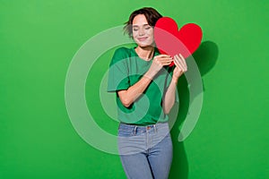Photo of lovely positive girl closed eyes hold large heart card isolated on green color background