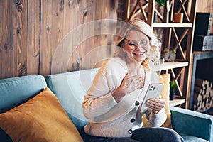 Photo of lovely retired woman sit sofa touch chest hold gadget dressed casual outfit cozy home interior living room in