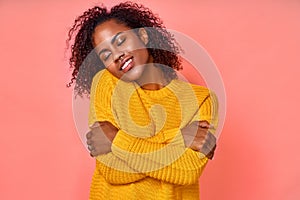 Photo of lovely smiling black woman embraces herself, has high self esteem, closes eyes from enjoyment, likes her new photo