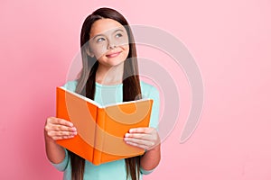 Photo of lovely sweet little ponderous latin lady long hairstyle arms hold orange book sly look up empty space