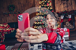 Photo of lovely young lady hold device plump lips video call dressed stylish red sweater christmas tree decorated