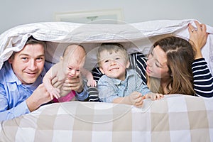 Photo of loving family four lying on white bed in morning.