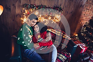 Photo of loving married couple wife husband sit sofa couch cuddle on christmas night in decor room indoors