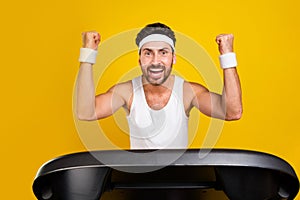 Photo of lucky cheerful guy activewear running treadmill rising fists screaming yes isolated yellow color background