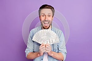 Photo of lucky funny young man wear jeans shirt holding arms hands money stack open mouth isolated violet color