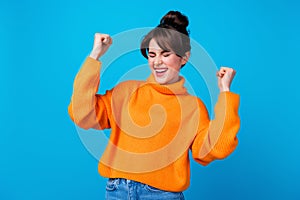Photo of lucky impressed woman dressed orange sweater closed eyes screaming yeah rising fists isolated blue color